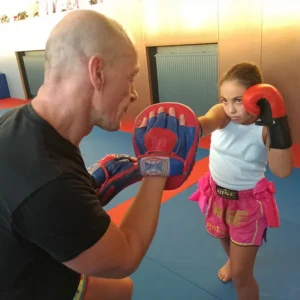 Une enfant frappe sur une patte d’ours, tenue par son entraîneur avec un air déterminé.