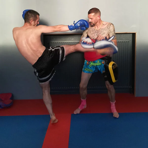 Un boxeur s'entraîne sur pao. Il envoie un middle kick avec une garde digne des boxer thaï.