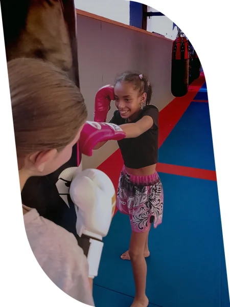 Deux enfants s’entraînent au sac de frappe avec un sourire enthousiaste.