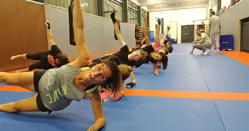 Un groupe de boxeuses de tous âges, alignées les unes derrière les autres, effectue des exercices de gainage des abdominaux du côté droit.